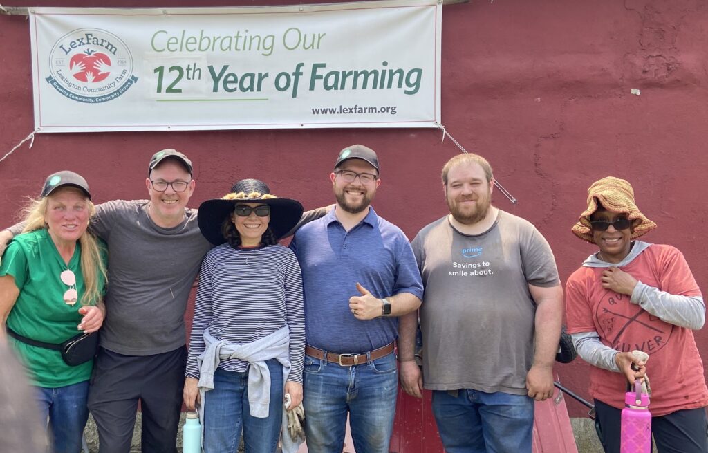 Six smiling people in caps and floppy hats standing in front of LexFarm banner