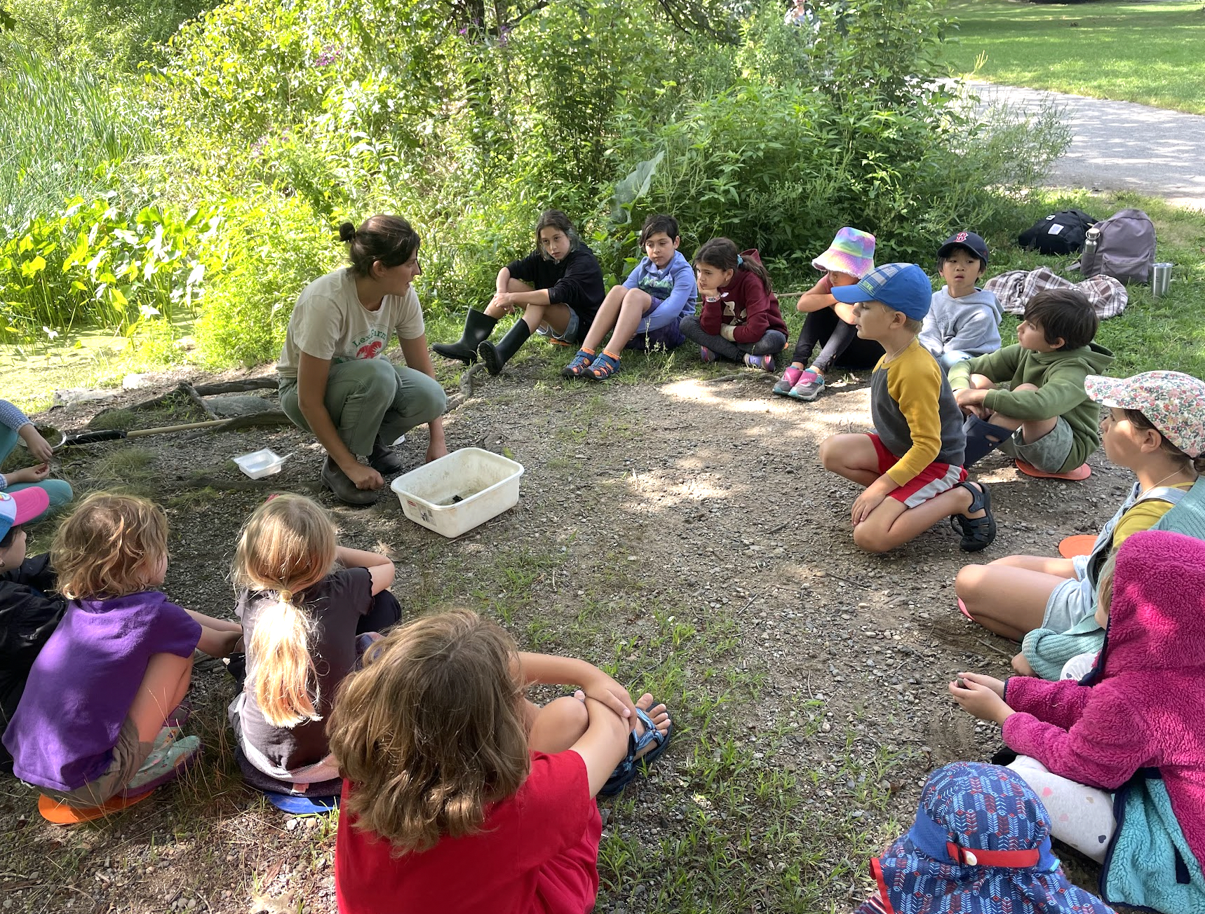 Screenshot children sitting on ground in circle watching teacher
