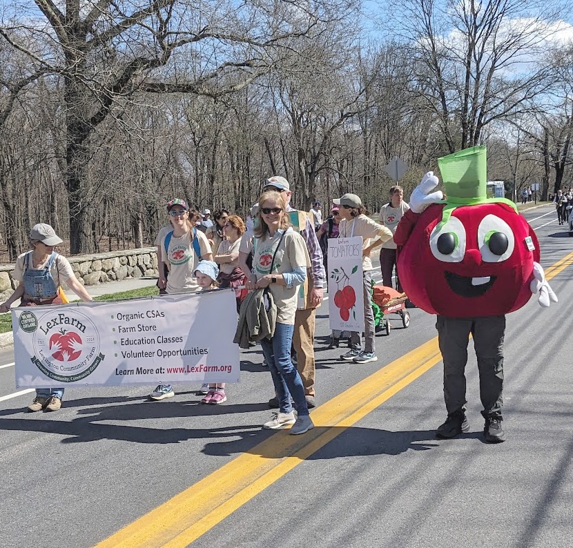 people marching down the street with LexFarm banner and red tomato mascot
