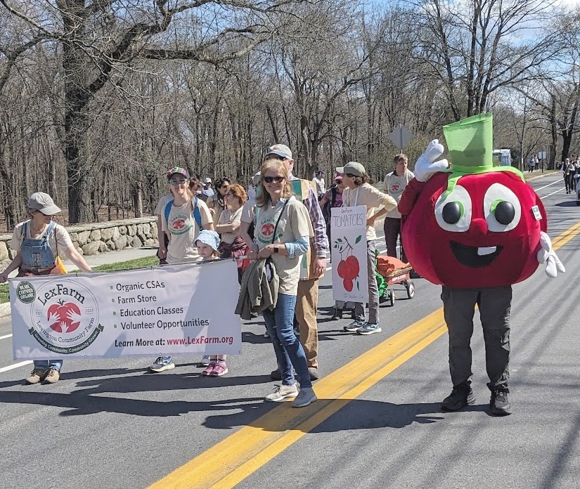 people and tomato mascot marching with the LexFarm banner in the parade